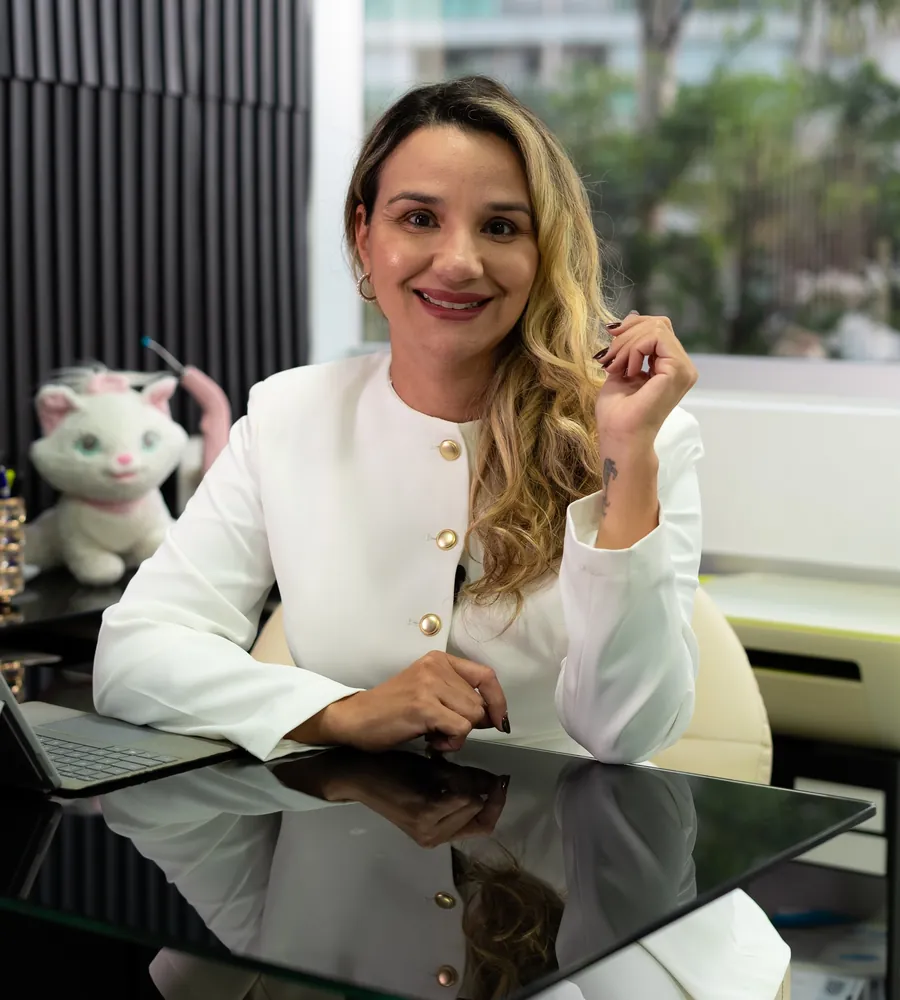 Dra. Érica Mello sorrindo em sua mesa no consultório